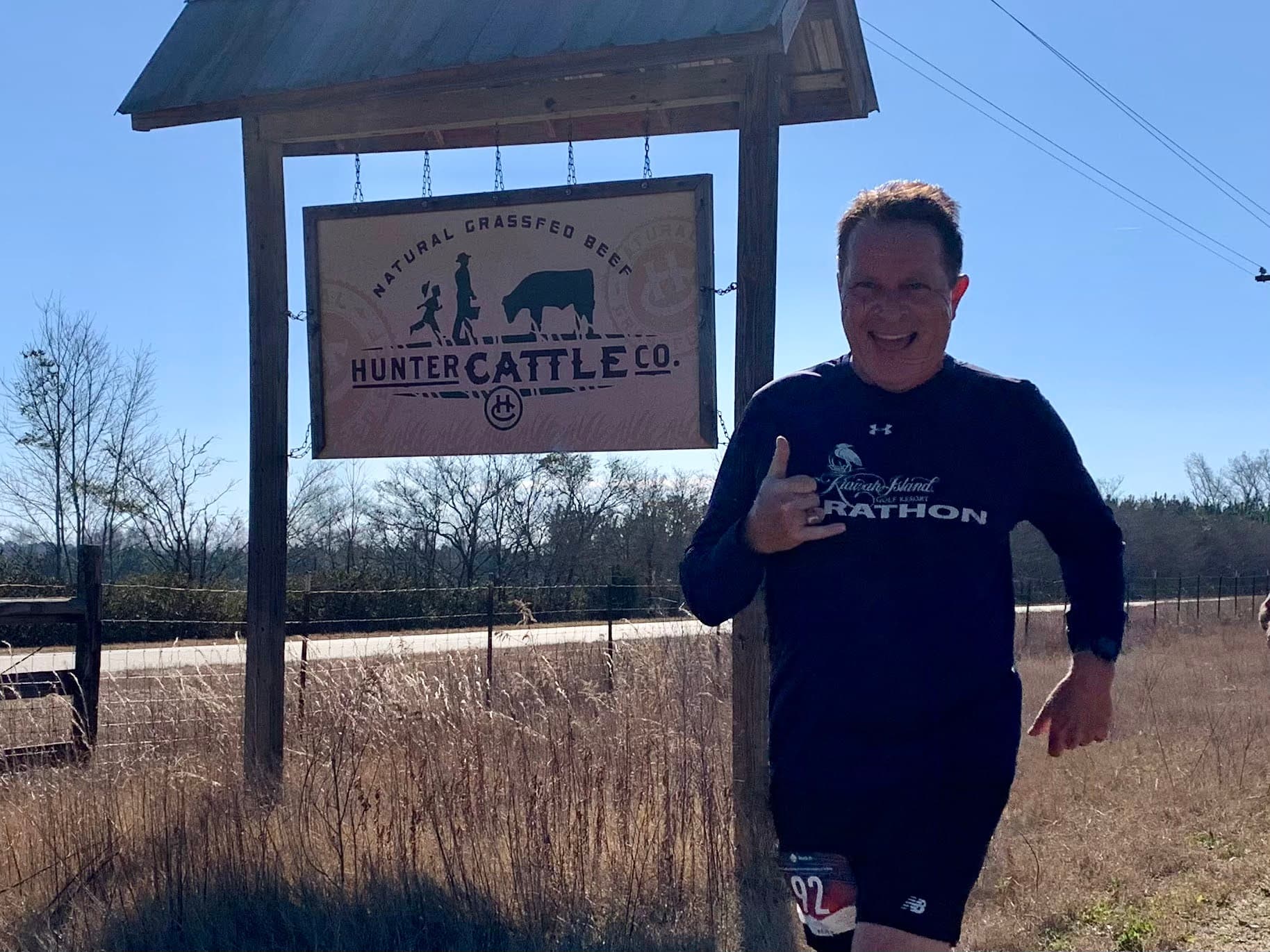 Runner giving thumbs up at Hunter Cattle Co sign
